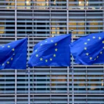 Bandeiras da União Europeia em frente a uma fábrica, destacando gigafábricas de IA