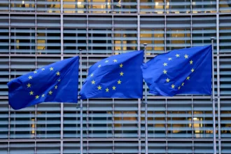 Bandeiras da União Europeia em frente a uma fábrica, destacando gigafábricas de IA